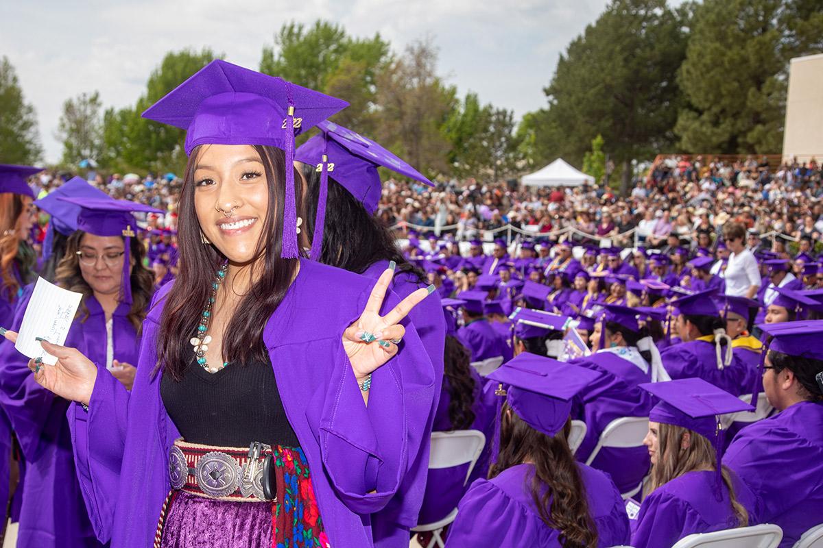 female native graduate smiles and flashes a peace sign at graduation